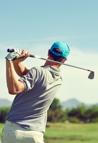 Golfer hitting golf shot with club on course while on summer vacation